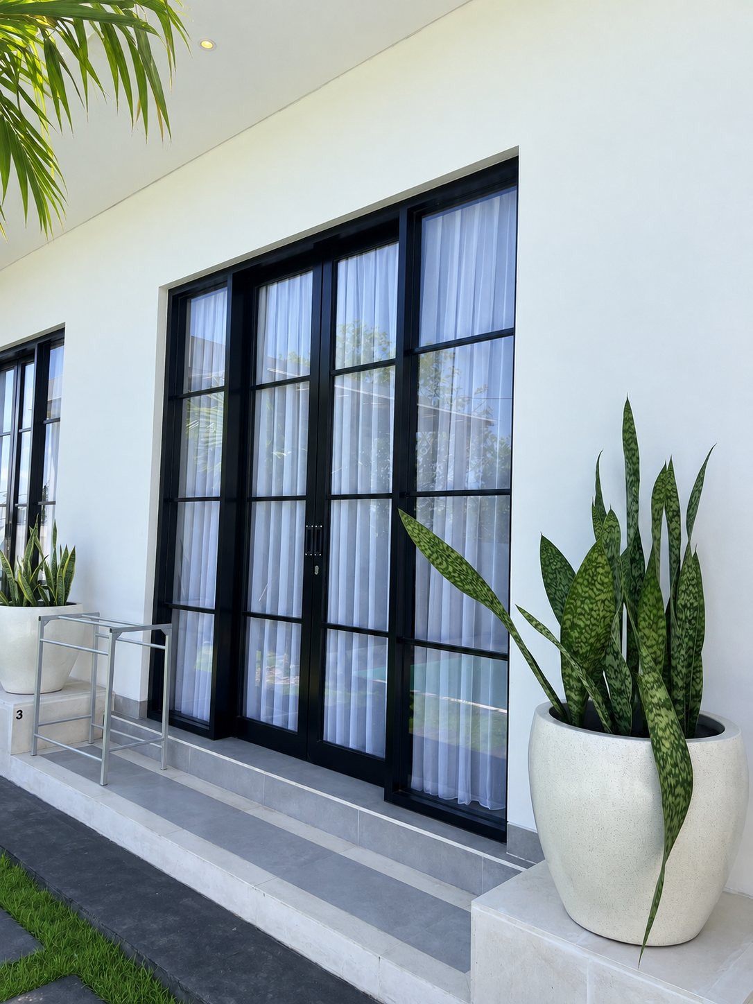 Guest room with black-framed glass doors, sheer curtains and potted snake plants on the terrace