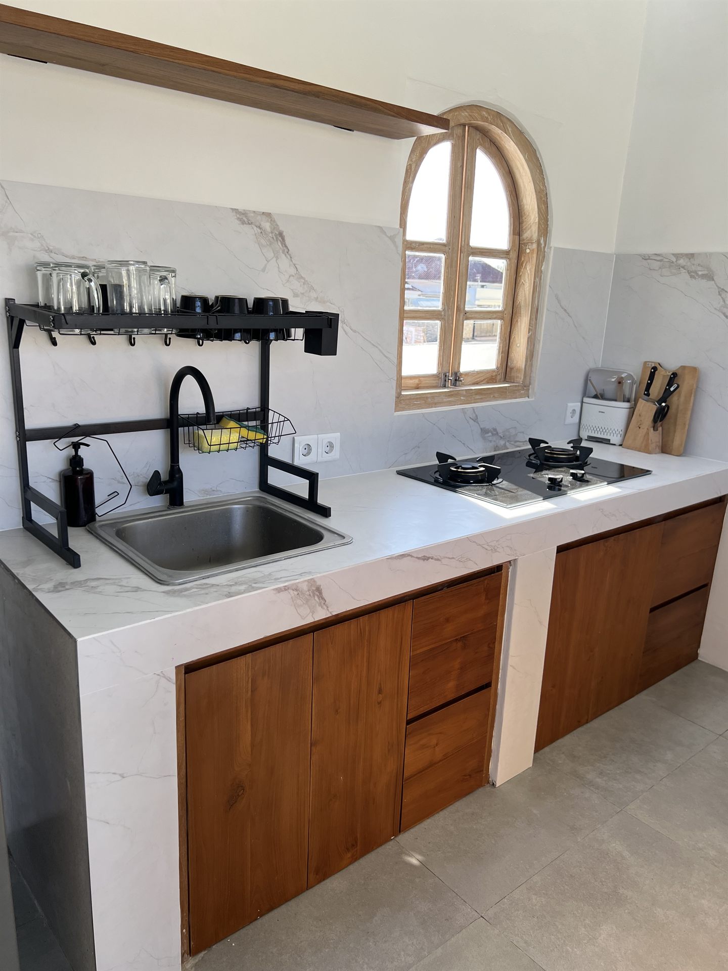 Kitchen sink and gas stove with a marble backsplash, teak cabinets and an arched window
